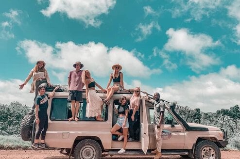 A group of people sit or stand around a safari jeep.