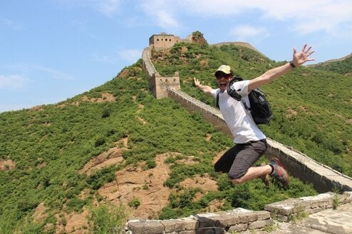 A man jumps in the air smiling on the Great Wall of China.